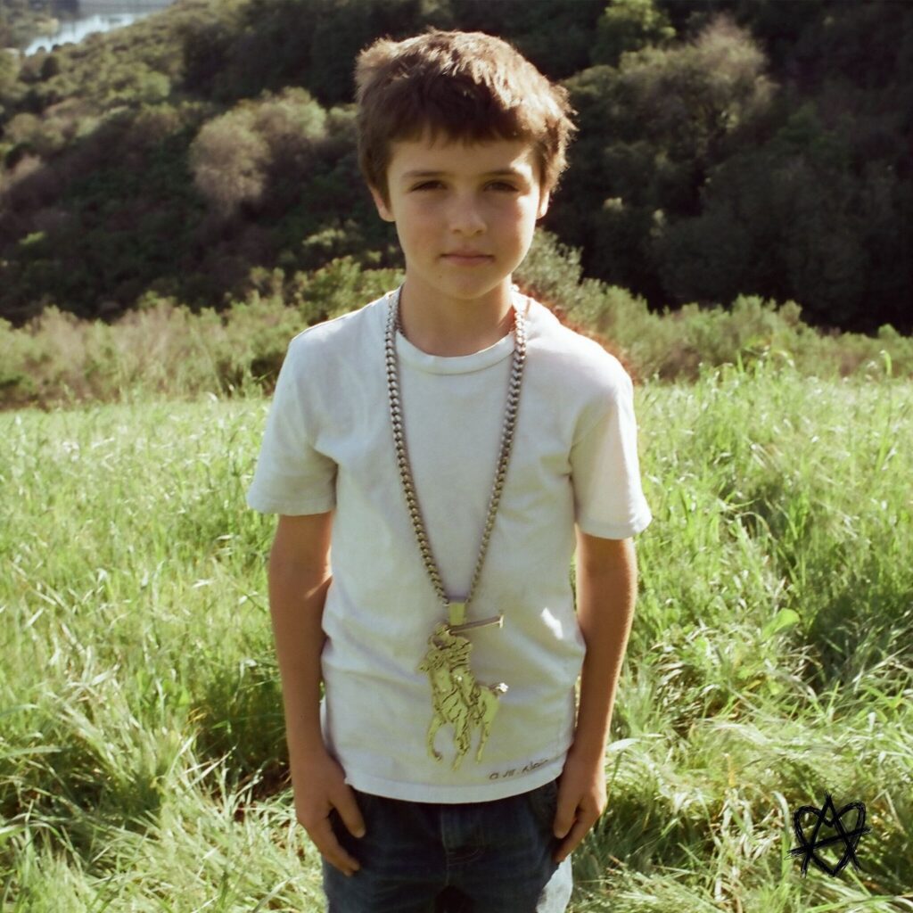 Image may contain Clothing TShirt Accessories Jewelry Necklace Grass Plant Child Person Face and Head